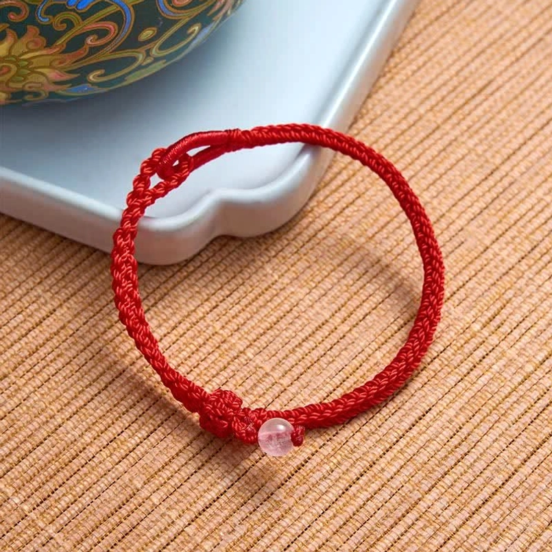Pink rose quartz red string bracelet with adjustable clasp on woven mat and ceramic tray