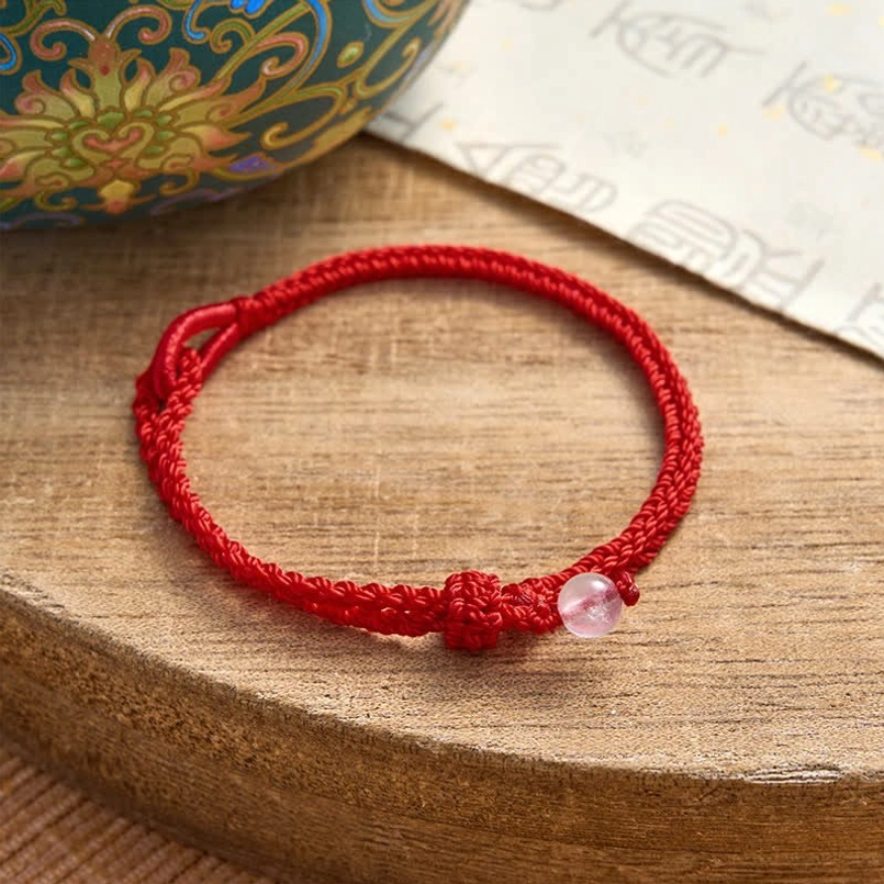 Rose quartz red string bracelet on wooden table with oriental decor and decorative knot