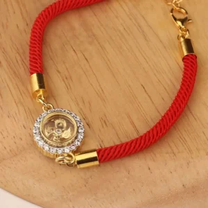 Red string feng shui rotatable windmill bracelet with copper brass charm and cubic zirconia on wooden surface