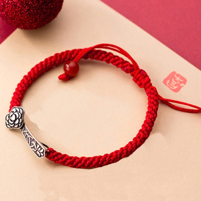 Red string Ruyi bracelet with traditional Chinese seal decoration on red and beige stationery background