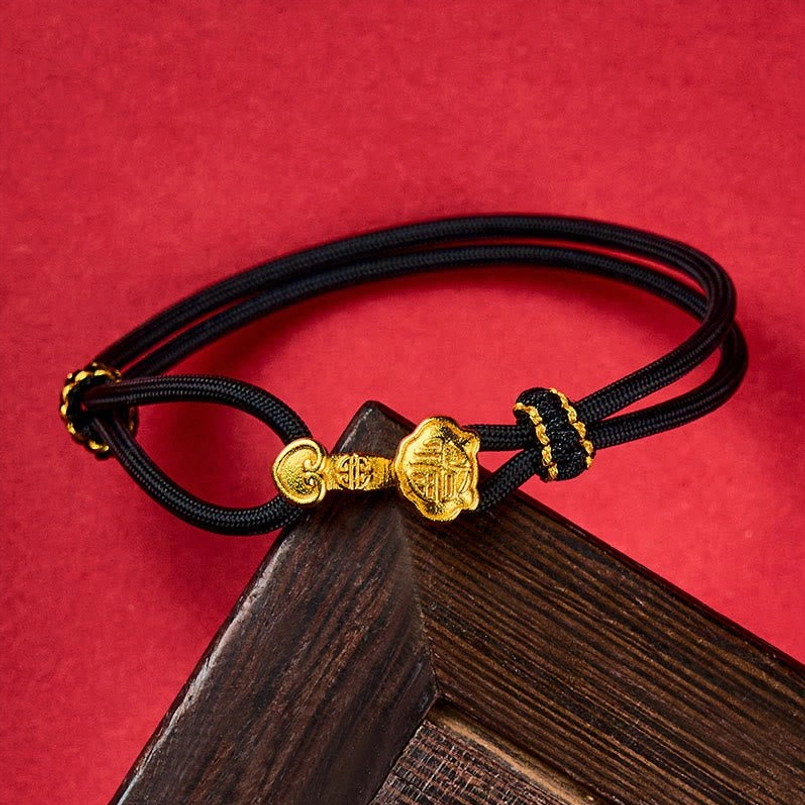 Black braided cord bracelet with Ruyi shaped gold hardware, wooden decorative background