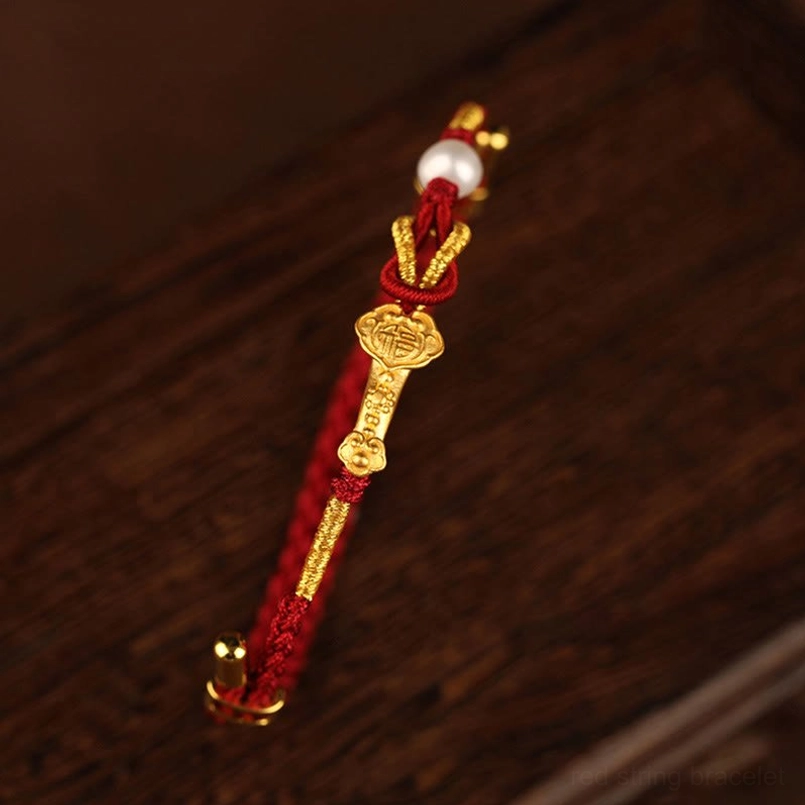 Red string bracelet with gold accents and white pearl being worn on adult wrist close-up view