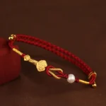24K gold Ruyi Fu rabbit pearl red string bracelet with intricate braided knot design on dark fabric