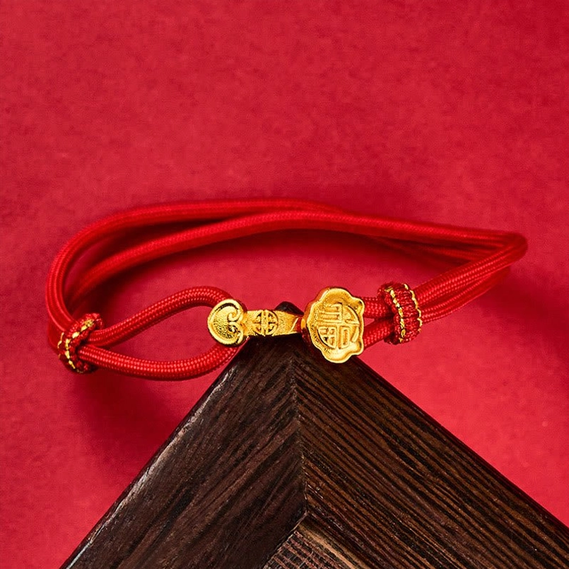 Adjustable red cord bracelet with braided knot, gold Ruyi charm detail, wooden background accent