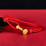 Red string bracelet with Ruyi Fu gold charm, adjustable woven knot design, displayed on red background