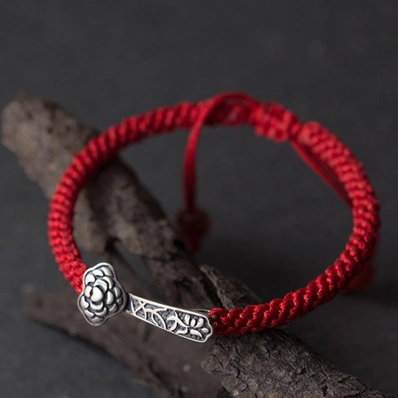 Sterling silver Ruyi red string bracelet displayed on dark wood branches, side overhead angle