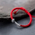 925 sterling silver Ruyi red string bracelet with embossed charm on dark slate background, side overhead view