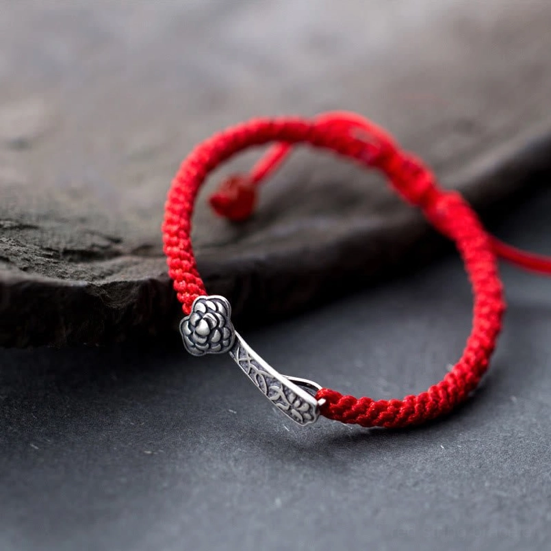 925 sterling silver Ruyi red string bracelet with embossed charm on dark slate background, side overhead view