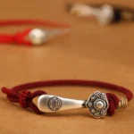 999 sterling silver Ruyi stick protection bracelet with wine red cord - overhead close-up view showing intricate braiding and detailed silver charm