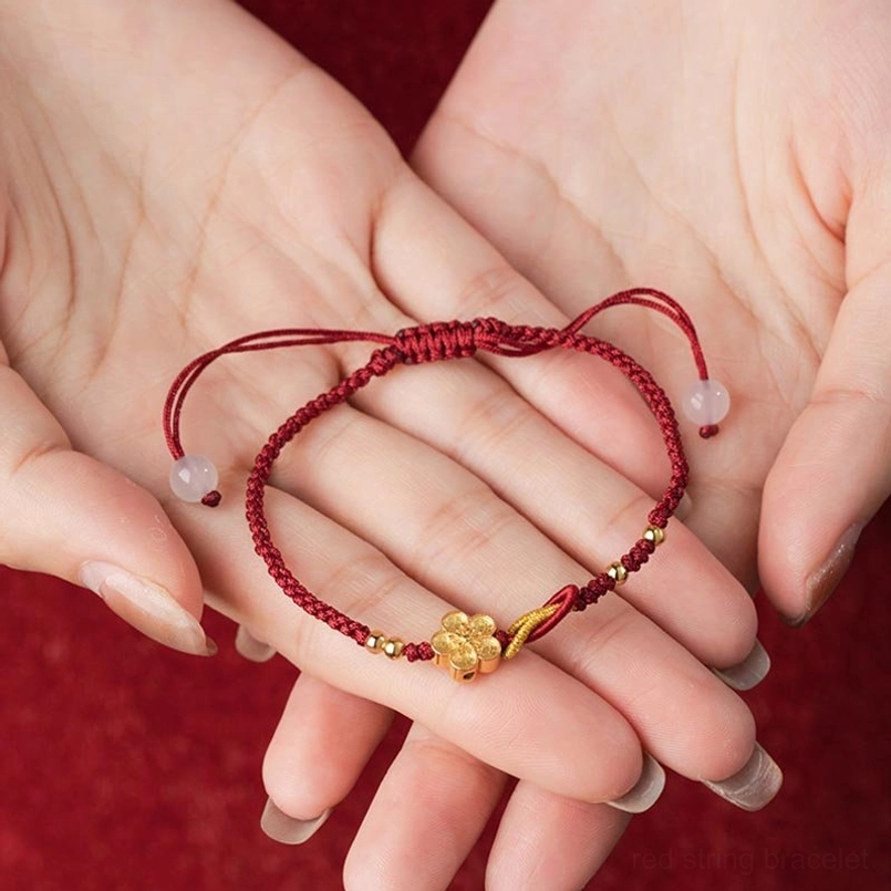 Sakura red string bracelet displayed on open human palms red fabric background