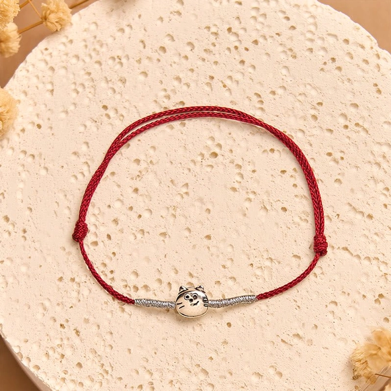 Silver red string cat charm bracelet with braided cord and decorative stone background