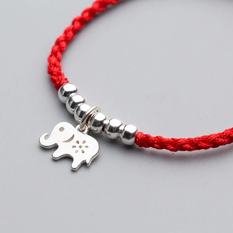 Close-up side view of engraved silver elephant and silver beads on red woven bracelet