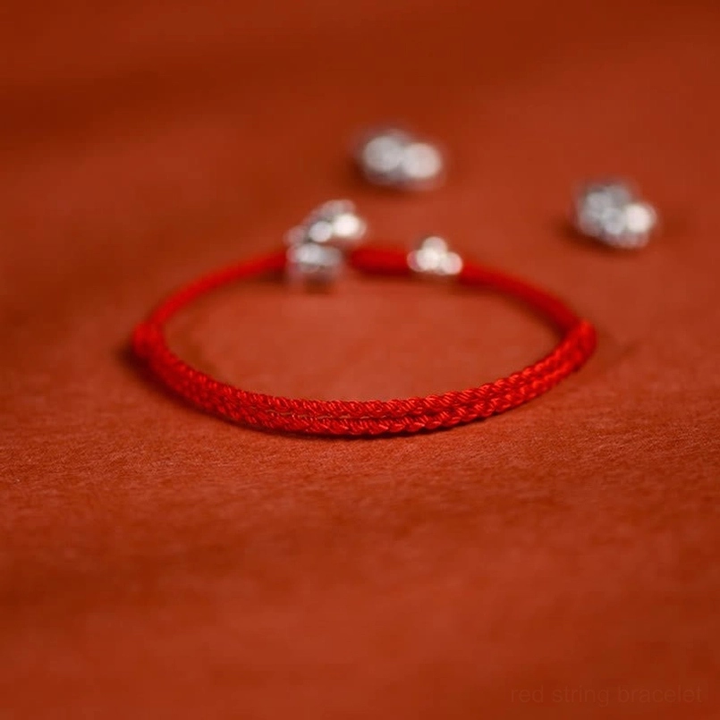 Sterling silver horse pendant and bell charm on braided red rope bracelet low angle shot