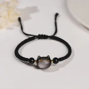 Silver Sheen Obsidian cat protection bracelet with black woven cord and gold accent details, top-down flat lay view
