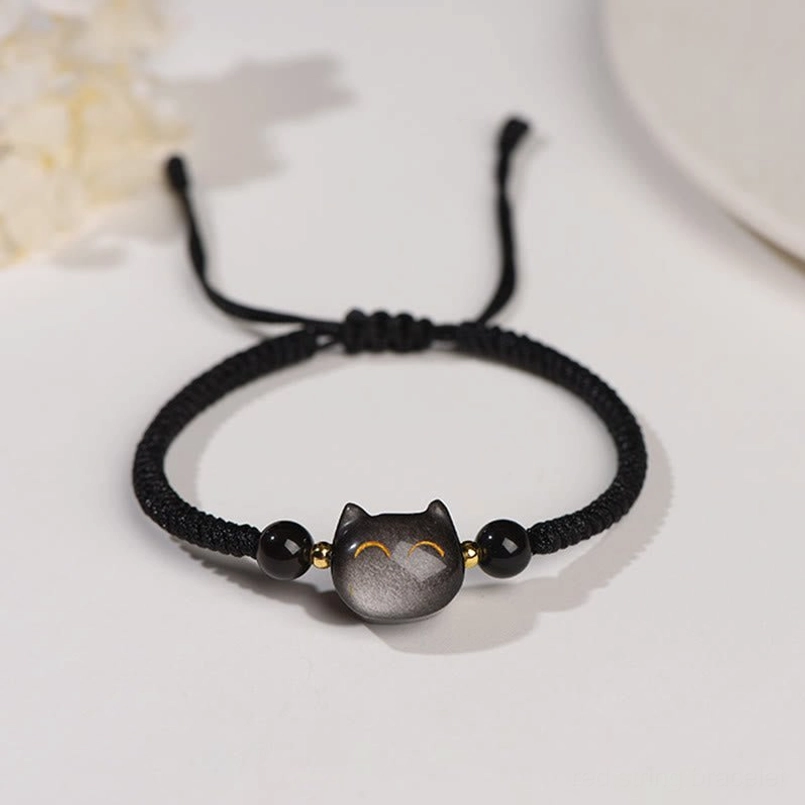 Silver Sheen Obsidian cat protection bracelet with black woven cord and gold accent details, top-down flat lay view