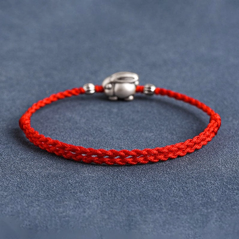 Silver rabbit red string bracelet full length flat lay showing braided cord texture