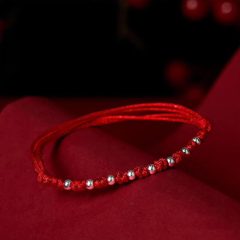 Sterling silver red cord bracelet with evenly spaced metal beads displayed on red fabric background