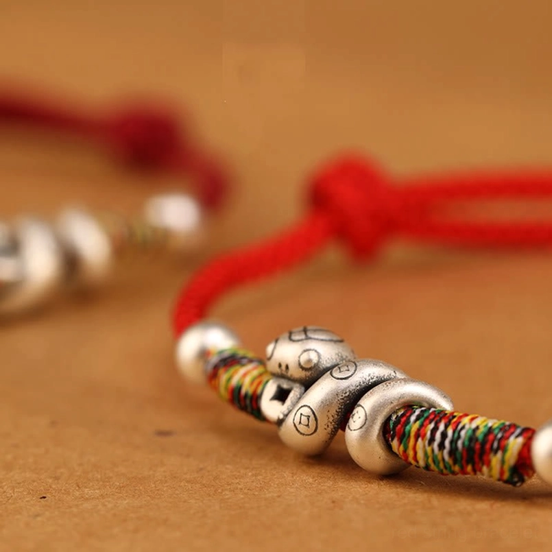Macro close-up of sterling silver snake charm and colorful woven wrapping with round silver spacer beads on red string anklet