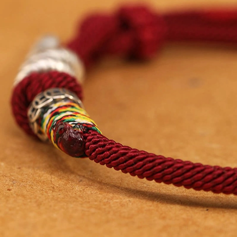 Close-up detail of silver snake charm and multicolored woven cord accents on red string bracelet