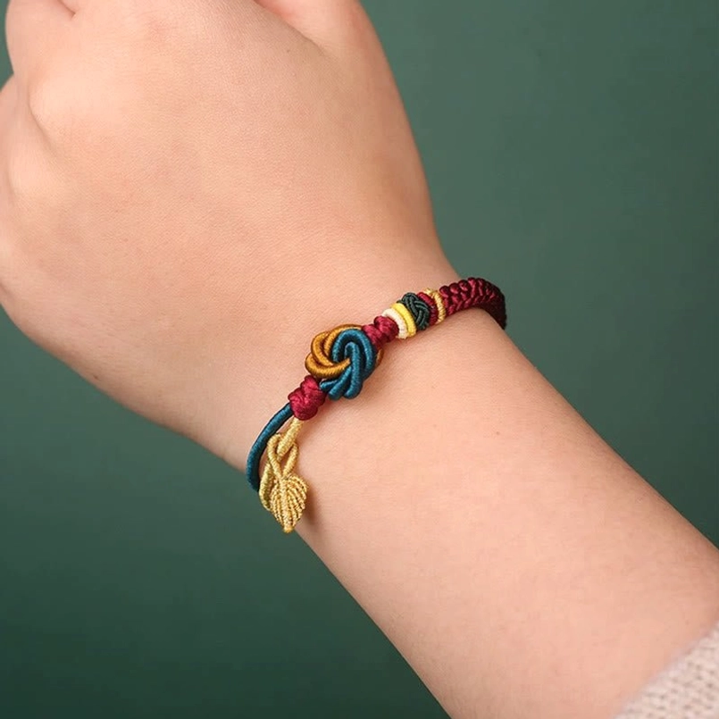 Slim braided Tibetan luck bracelet on wrist close-up with knot decor and golden leaf