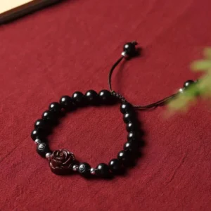 Small leaf red sandalwood red string bracelet with rose charm flat lay on red fabric
