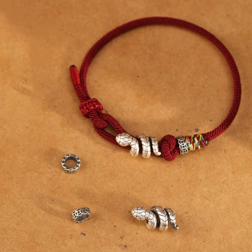Red string snake bracelet with loose silver snake charms and metal rings display, flat lay