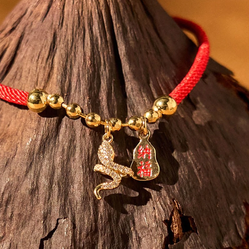 Snake charm red fortune bracelet close-up side view on rough wooden background