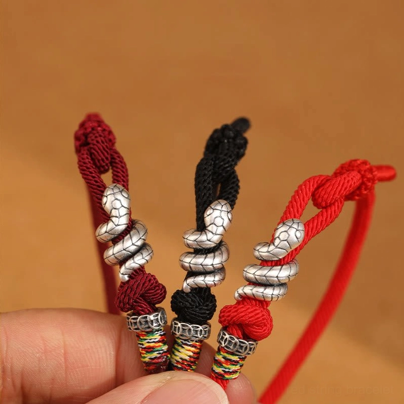 Multiple handmade red string snake bracelets in assorted colors with silver charms, hand-held close-up