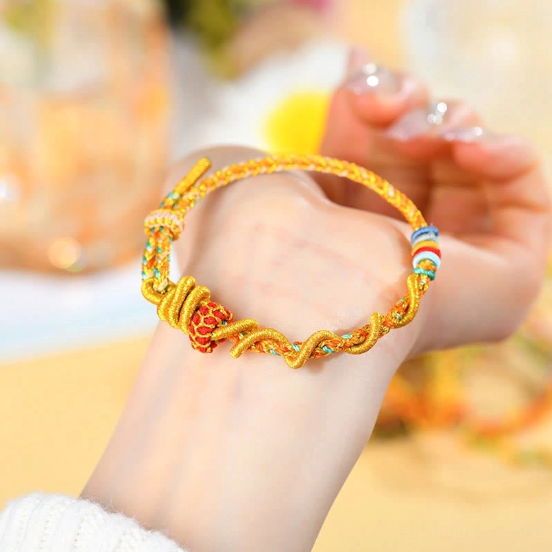 Hand-held Year of the Snake luck bracelet showing twisted gold braided cord and red-gold knot