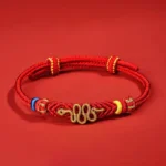 Year of the Snake red string protection bracelet with eight thread peace knot and gold snake charm, overhead flat lay view