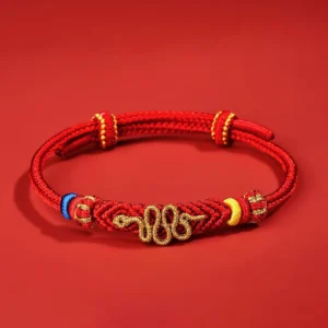 Year of the Snake red string protection bracelet with eight thread peace knot and gold snake charm, overhead flat lay view
