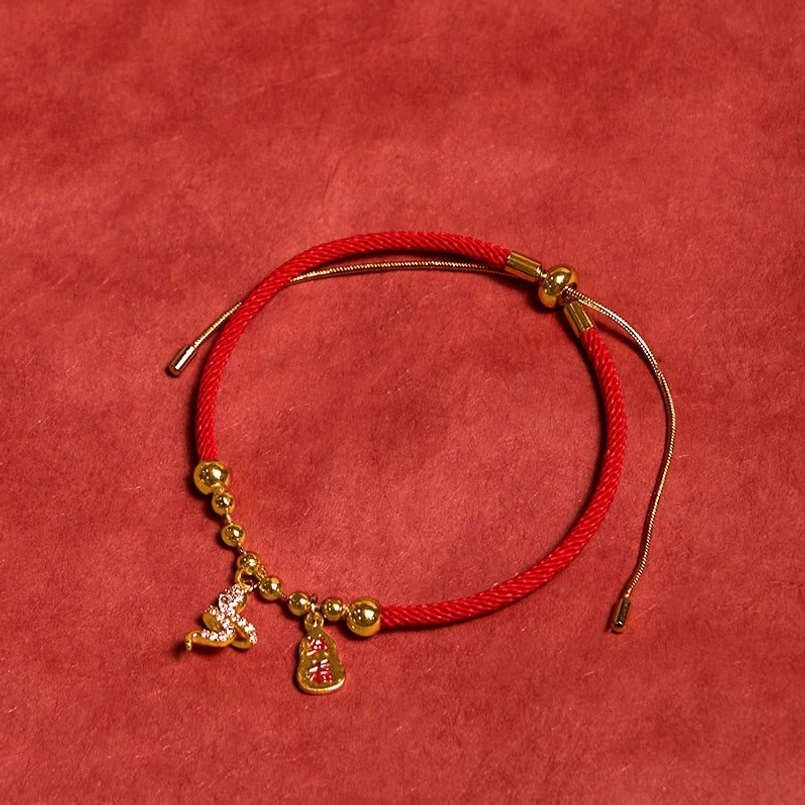 Snake themed red string fortune bracelet top view on solid red fabric background