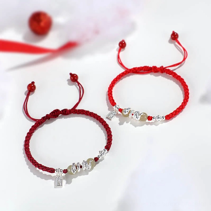 Two snake year red string bracelets with jade beads and silver tags flatlay