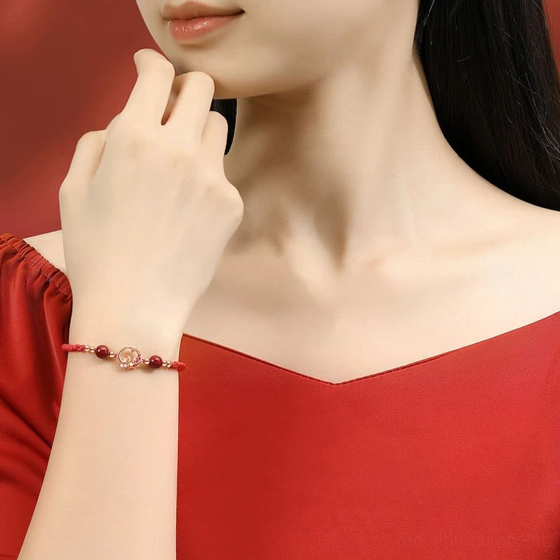 Worn year of snake red string jade protection bracelet on wrist with gold charm detail close-up