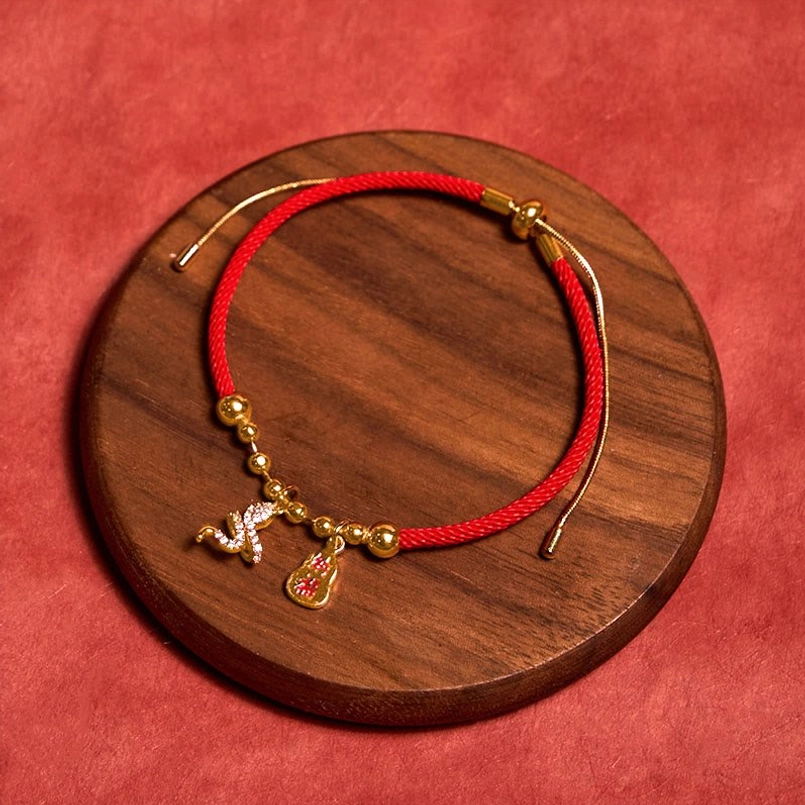Snake zodiac protection braided red string bracelet flat lay on wooden coaster red backdrop
