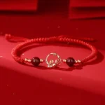 Year of Snake red string protection bracelet with cinnabar beads and gold snake koi charm, flat lay top view