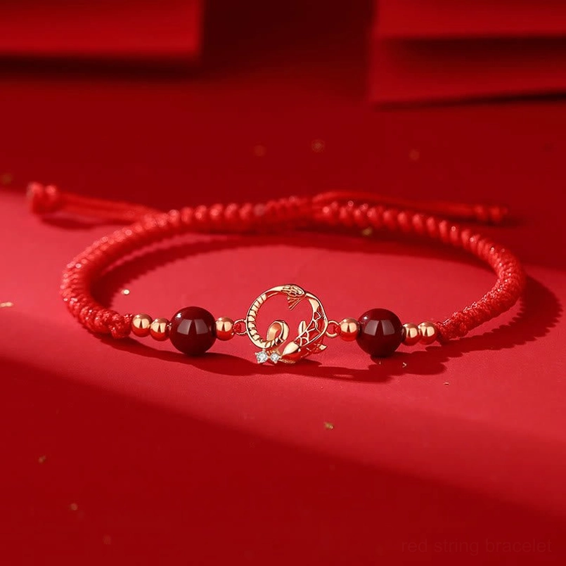 Year of Snake red string protection bracelet with cinnabar beads and gold snake koi charm, flat lay top view