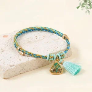 Five-color Song Brocade red string bracelet with blue and yellow woven cord and turquoise tassel featuring lucky charm pendant on stone background