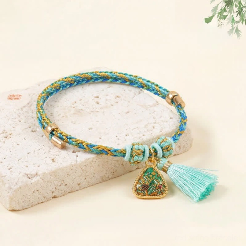 Five-color Song Brocade red string bracelet with blue and yellow woven cord and turquoise tassel featuring lucky charm pendant on stone background