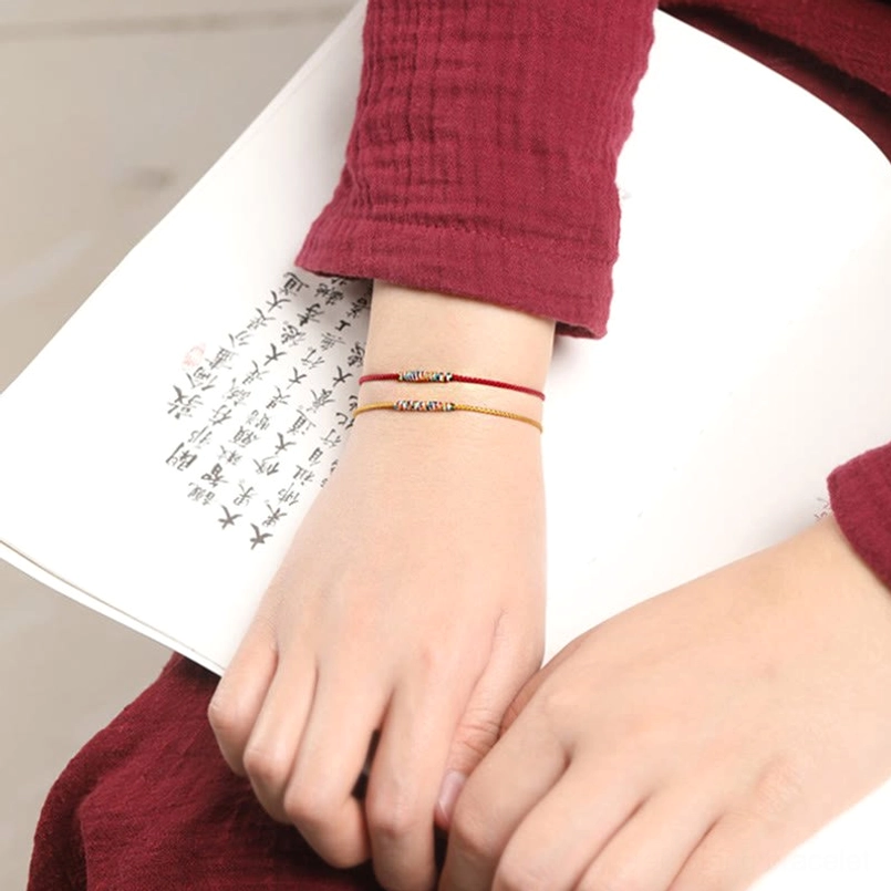 Lifestyle image of stacked thin Tibetan braided bracelets on wrist with Chinese calligraphy background