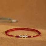 925 sterling silver red string bracelet with engraved beads and gold accents on brown fabric background