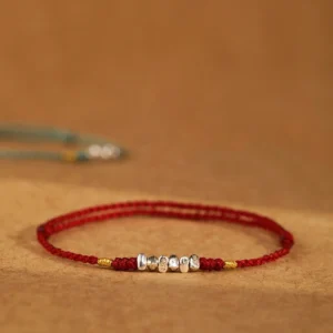 925 sterling silver red string bracelet with engraved beads and gold accents on brown fabric background