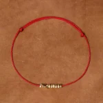 Red braided string bracelet with gold silver accents on leather background flat lay