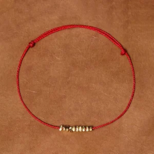 Red braided string bracelet with gold silver accents on leather background flat lay