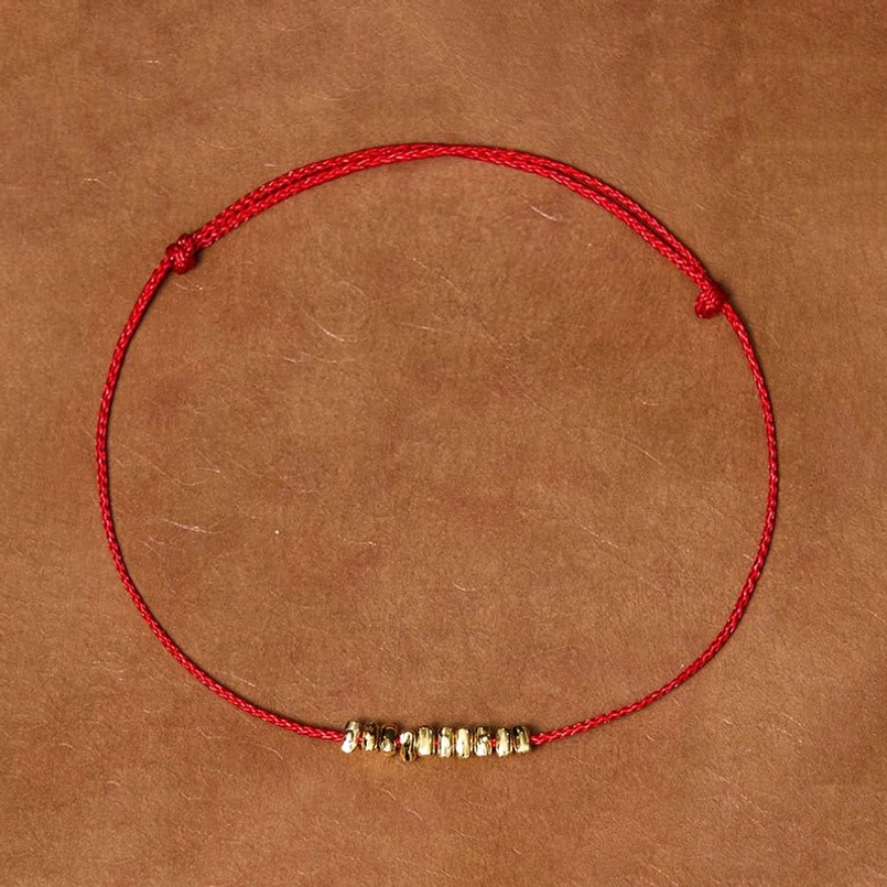 Red braided string bracelet with gold silver accents on leather background flat lay