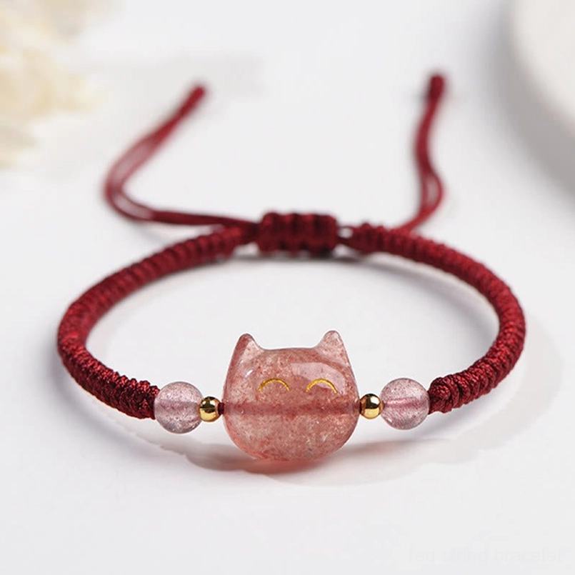 Strawberry Quartz cat protection bracelet with red cord and pink quartz cat charm, flat lay with floral decor