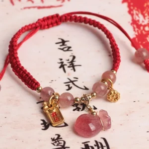 Natural strawberry quartz lotus red string bracelet flat lay with calligraphy background showing braided red cord, pink quartz stone, gold lotus charm and money bag pendant
