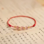 Strawberry quartz red string anklet with three pink crystal beads and gold spacers on calligraphy background
