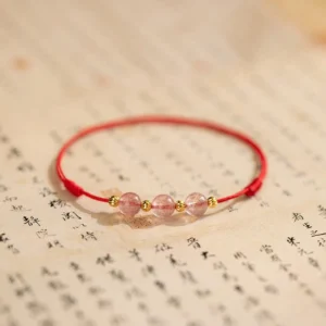 Strawberry quartz red string anklet with three pink crystal beads and gold spacers on calligraphy background