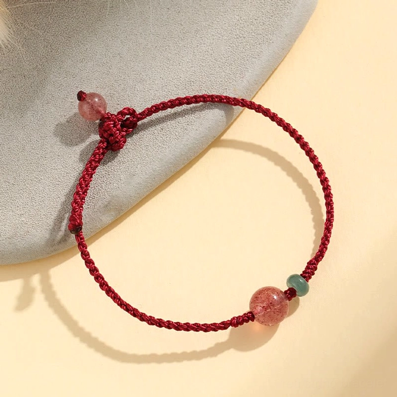 Side view of strawberry quartz and jade red string bracelet on beige mat